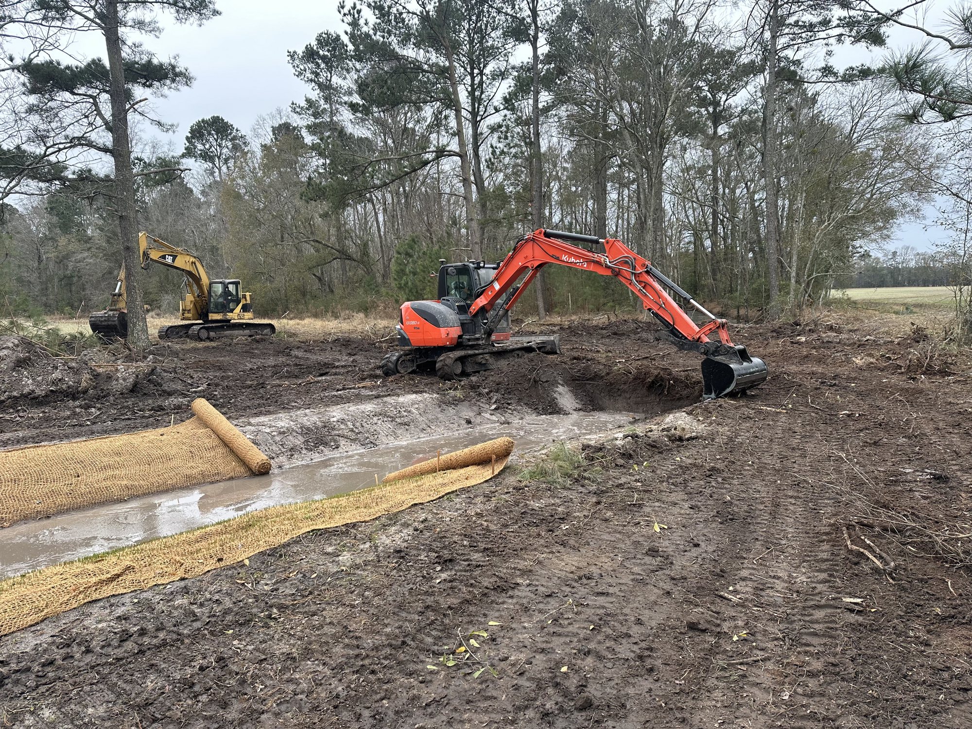 Excavators shaping a stream channel beside installed erosion matting