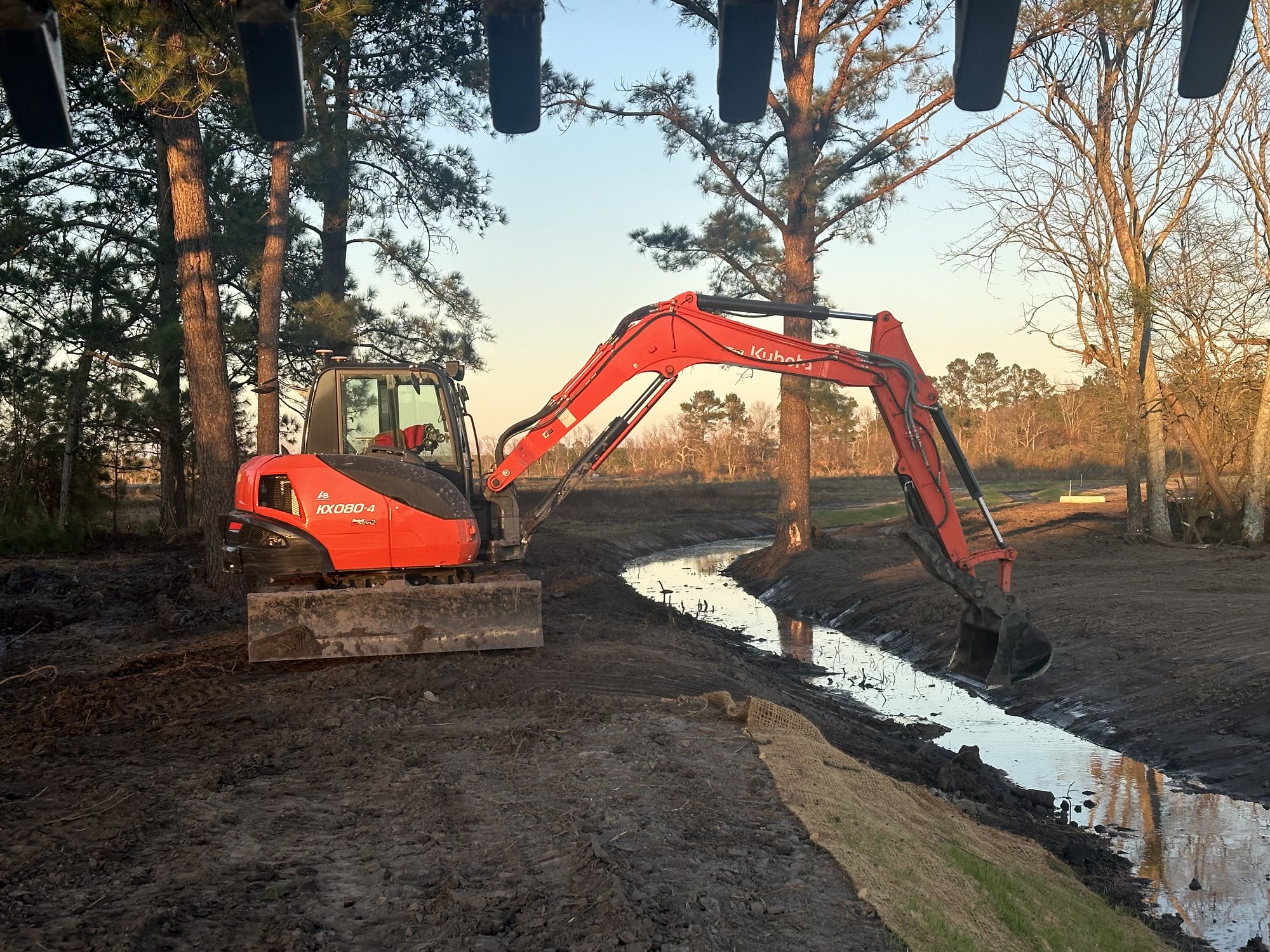 Excavator beside a freshly shaped stream channel in evening light